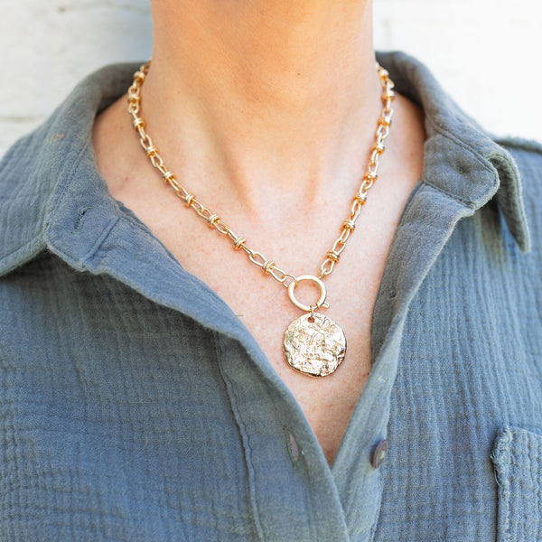 Woman wearing a gold chain necklace with a gold circular piece attached to it