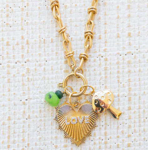 Picture of gold toggle chain with large gold heart pendant with the word "Love" in diamonds on it. Also attached is a green bead charms and a gold mushroom charm.