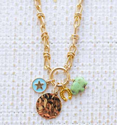 Picture of gold toggle chain with a gold disc pendant, a blue disc charm with a gold star in the center, a gold horseshoe and a green elephant.