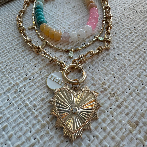 Picture of a stacked necklace set. of three. First is a pink, white, tan and green beaded necklace, second a delicate gold necklace with small gold tab beads and the main necklace is a chunky link necklace with a large gold heart pendant and a smaller white pendant that reads 11:11