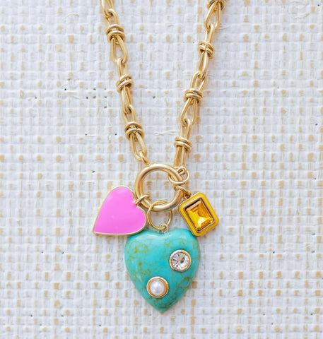 Picture of gold toggle chain with a large gold turquoise stone pendant inlaid with a pearl and diamond.  Necklace also has a pink heart charm and a rectangle amber stone charm.