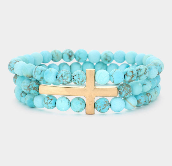 A blue gemstone bracelet stack with a gold cross 