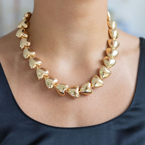 Woman wearing a gold necklace with gold puffed heart-shaped pendants