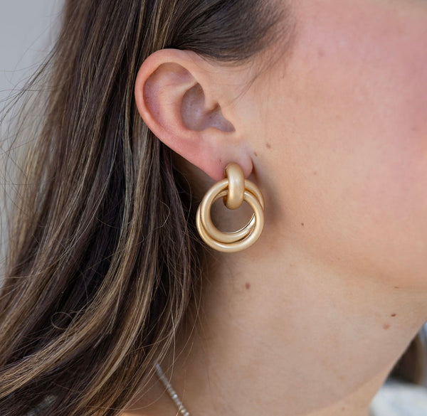 Model wearing brushed gold loops threaded to a smaller hoop.