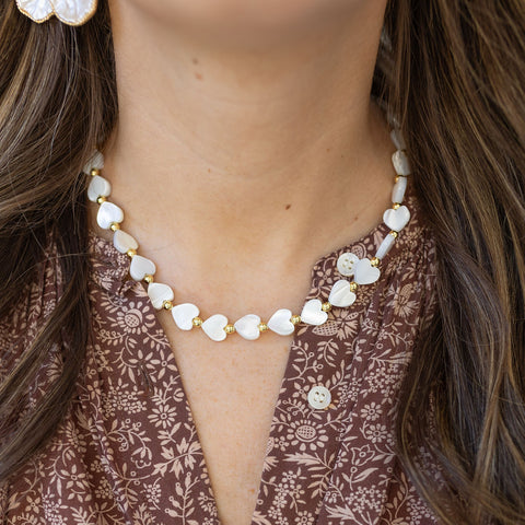 Model wearing short necklace made of white heart shaped beads and gold spacers.