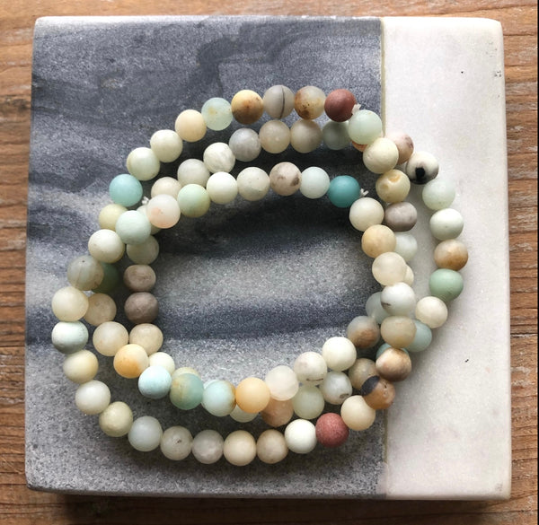 Picture of a set of three earth toned stone bead bracelets.  Beads have hues of turquoise, browns, ambers and off white colors.