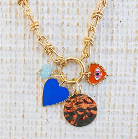 Picture of gold toggle chain with four charms attached: a light blue bead, blue heart, gold disc and red heart with an evil eye.