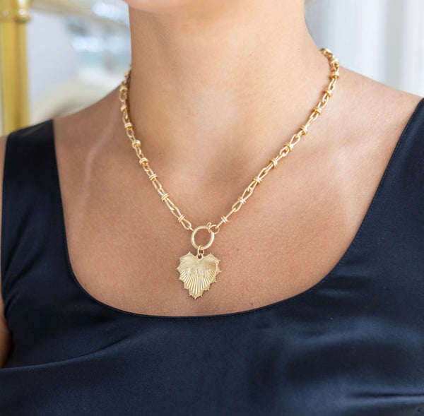 Woman wearing a gold chain toggle necklace with a gold heart medallion that says Love on it