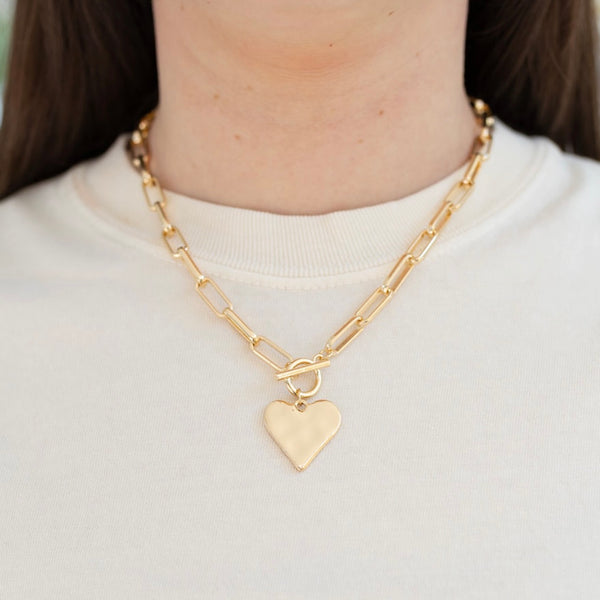 Picture of model wearing a gold toggle chain with a large gold heart pendant.