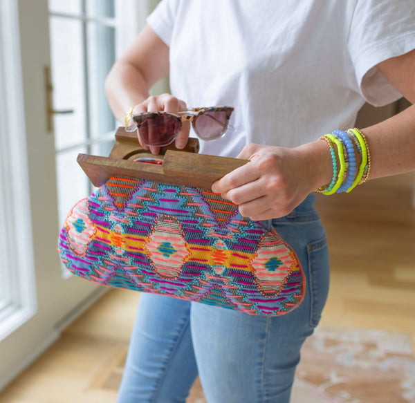 Person putting sunglasses in a clutch with brown at the top and a purple, orange, and yellow colored cloth design 