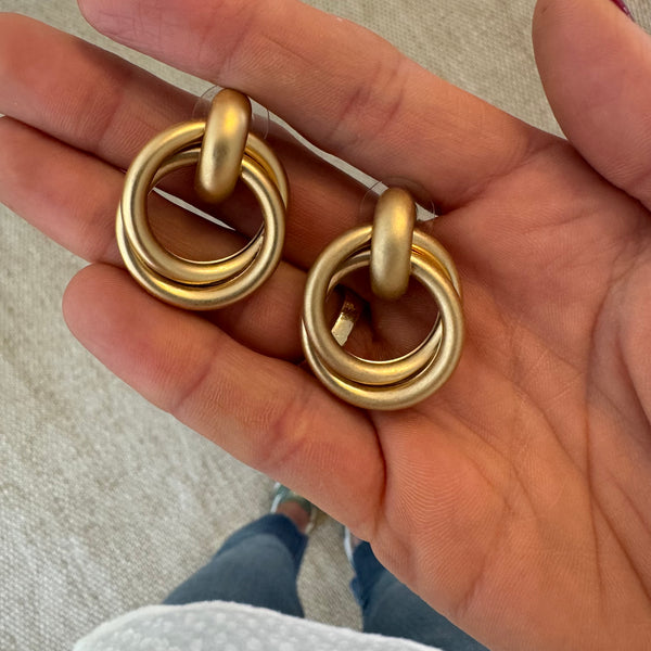 Picture of hand holding a set of brushed gold hoop earrings with gold loops wrapped through them.