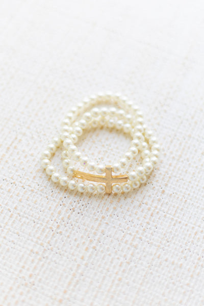 An image of a white bracelet stack with a gold cross