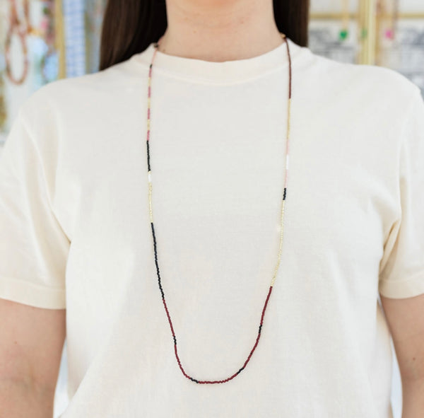 Picture of model wearing a long dark beaded necklace with white and gold accent colors.