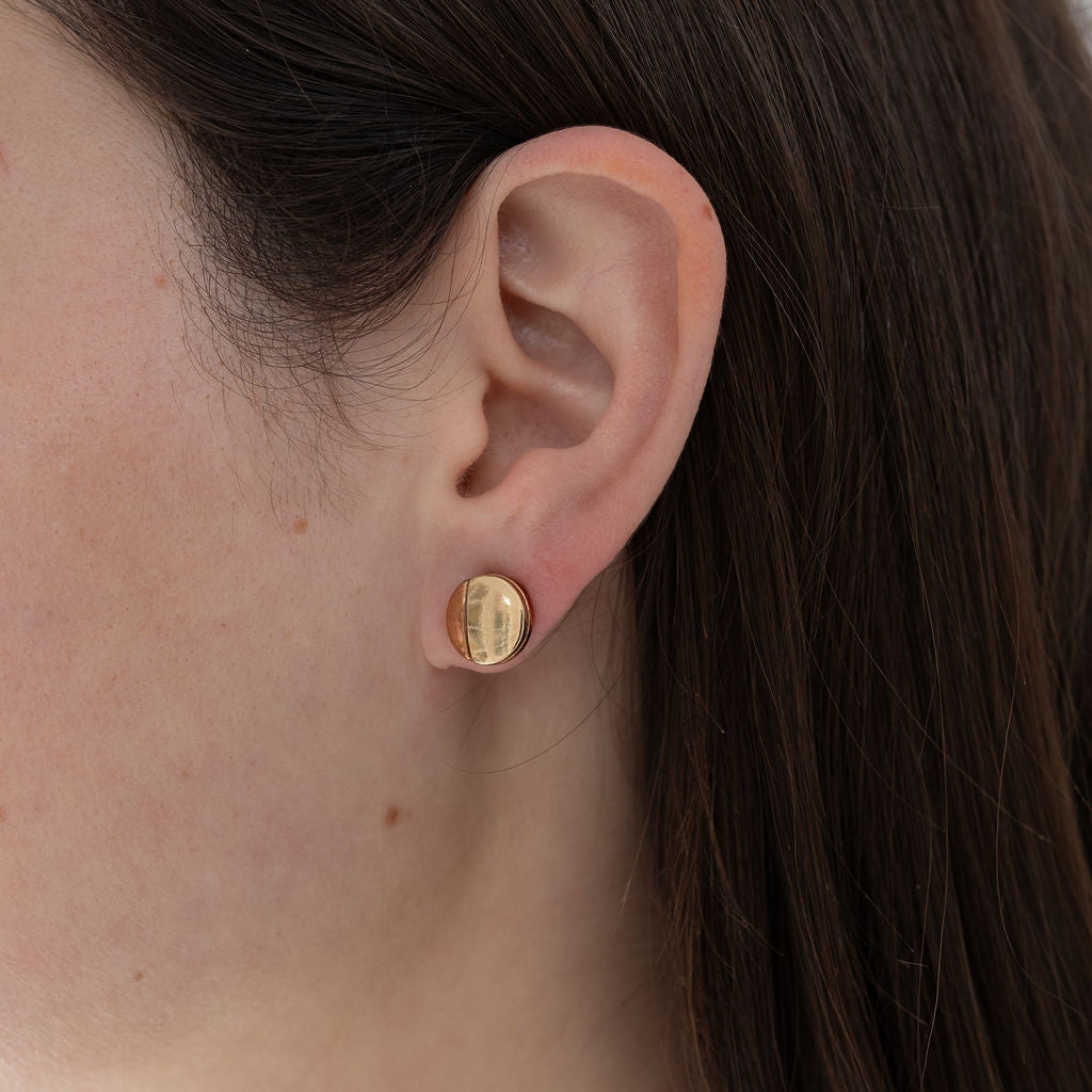 Picture of model wearing a small disc stud that is one third bronze and two thirds gold.