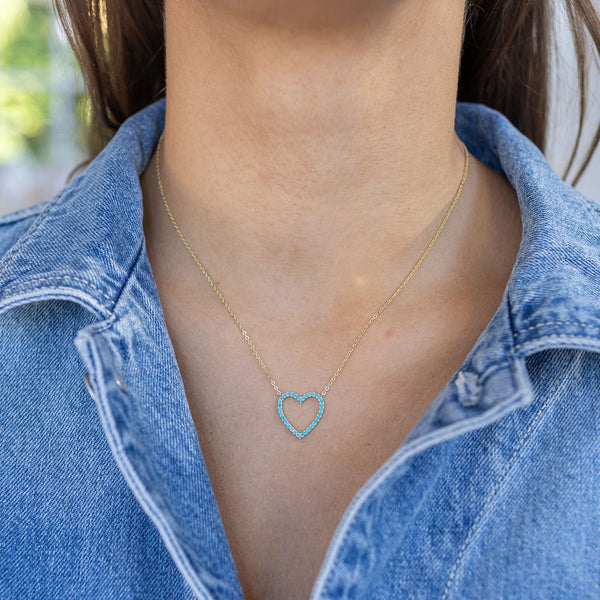 Model wearing a dainty gold chain necklace with blue heart pendant