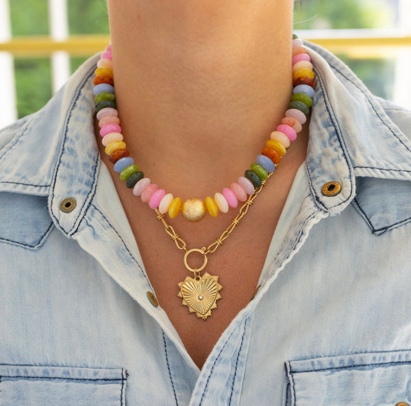 Model wearing chunky multicolored bead necklace stacked with a front clasping gold toggle chain necklace with heart pendant