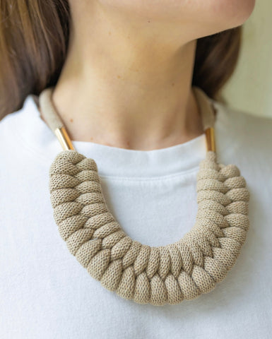 Woman wearing a big statement necklace with a light brown rope braid in the front and a gold link on the side