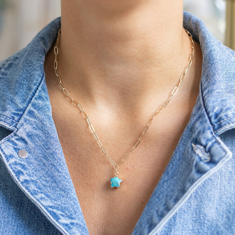 Woman wearing a thin paperclip gold chain necklace with a circle turquoise stone attached to it