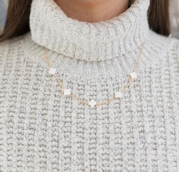 Model wearing a gold chain with five white four leaf clover flowers.