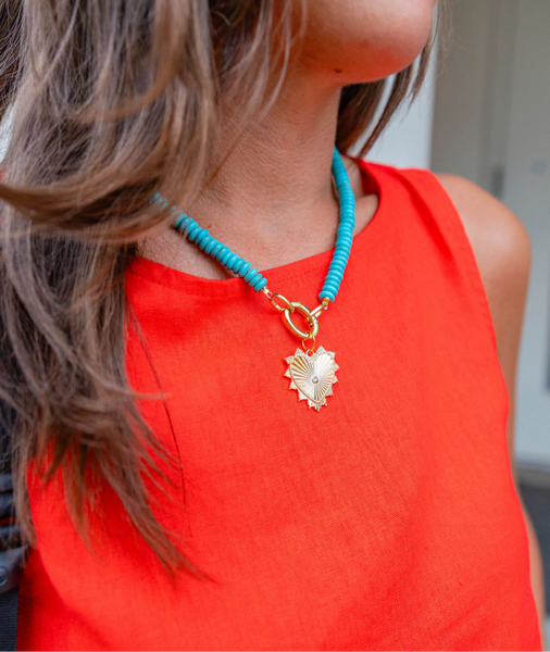 Woman wearing a big blue beaded necklace with a gold heart shape medallion attached to it