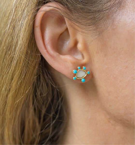 Girl wearing small earrings with a white/gold stone circular shape with tiny blue circular stones around it