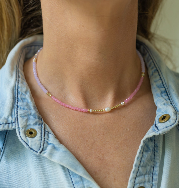 Woman wearing a thin necklace with small pink/purple/gold beads and pearls