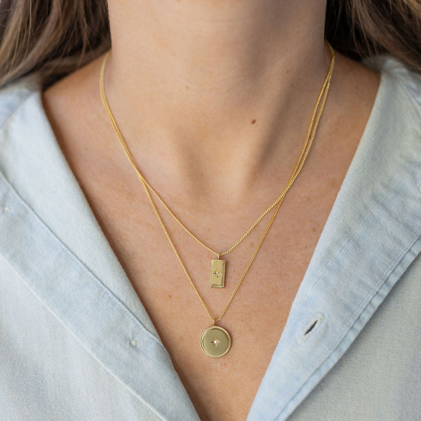 Model wearing stacked gold necklaces with rectangle and circular stone pendants