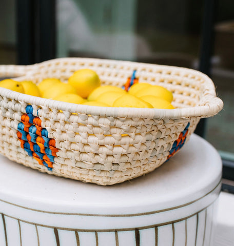 An image of a handmade cream basket with an orange/blue diamond design on each side holding yellow lemons