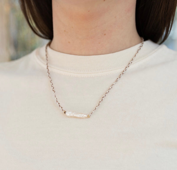 Picture of model wearing a brown and white braided necklace with an elongated fresh water pearl bead.