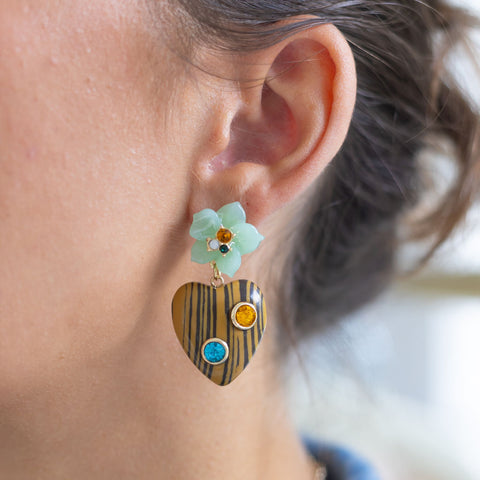 Woman wearing dangly earrings with light blue flowers and a gold heart attached to it