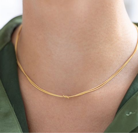 Model wearing dainty gold necklace with a petite knot in the center