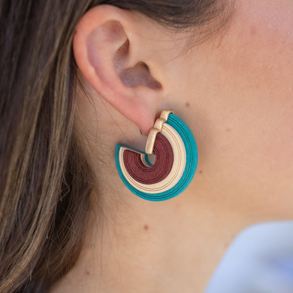 Model wearing chunky, textured teal, pale pink and maroon hoop earring