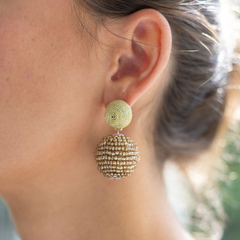 Woman wearing a beaded gold stud earring with a gold geometric shaped ball attached to it