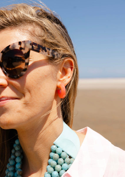 Girl wearing sunglasses at the beach smiling  looking away wearing a chunky orange earring
