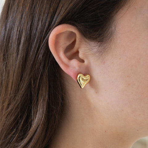 Picture of model wearing a gold heart earrings studs.