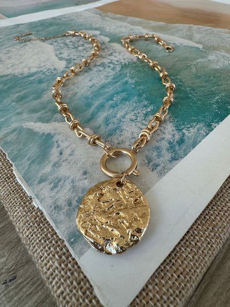 A gold chunky chained necklace sitting on a table with a large gold medallion attached to it