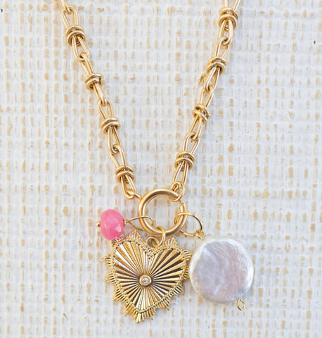 Picture of gold toggle chain with a gold heart pendant with a diamond in the center, large pearl disc and small pink bead charm attached.