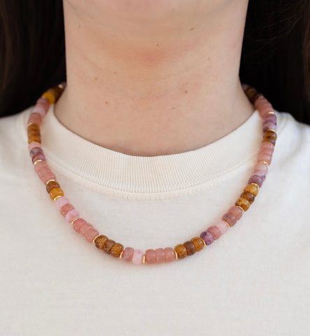 Picture of model wearing an earthy toned amber and rose pink beaded necklace with small gold beads.