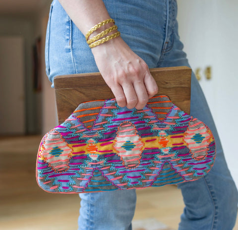Person holding in their hand a clutch with brown at the top and a purple, orange, and yellow colored cloth design 
