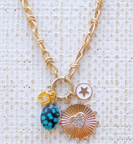 Picture of gold toggle chain with a gold horseshoe charm, a blue turquoise bead, and a white disc with a gold star in the center and gold disc with a diamond heart in the center.