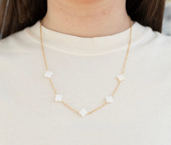 Picture of model wearing a gold necklace with five white four leaf clover flowers.