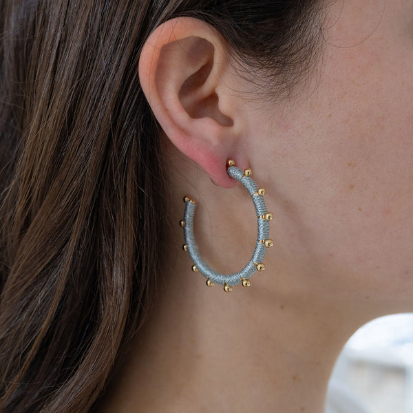 Picture of model wearing a blue string wrapped hoop earring with gold beads.