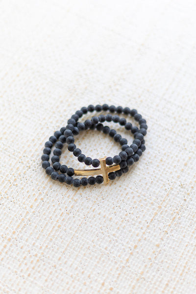 An image of a black bracelet stack with a gold cross