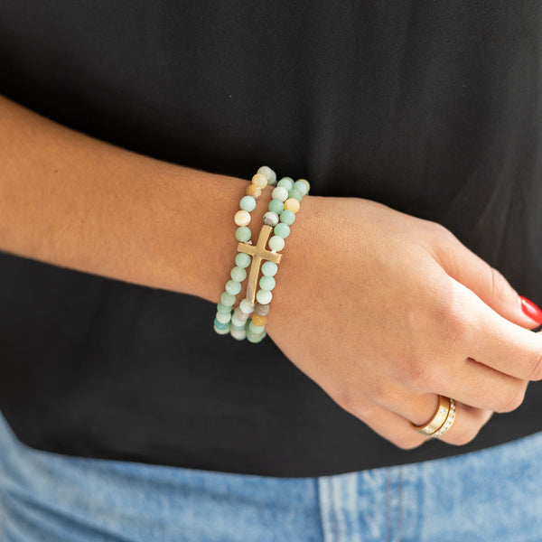 Woman wearing a light green gemstone bracelet stack with a gold cross on her wrist