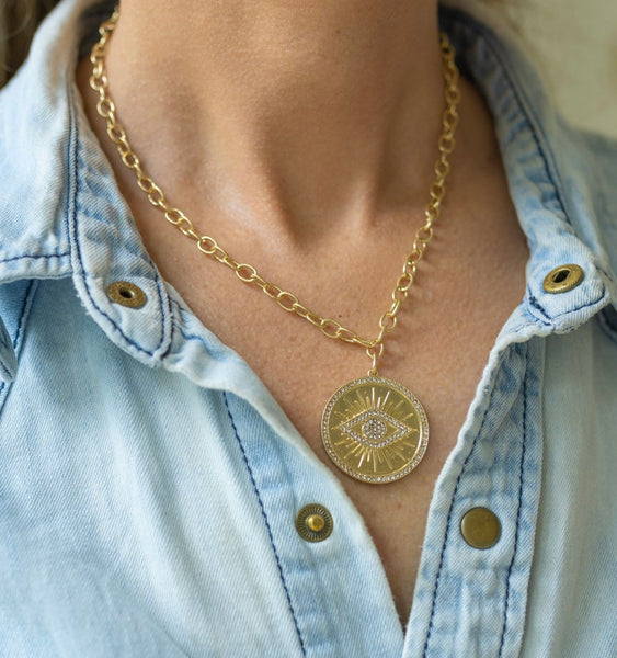 Woman wearing a necklace around her neck with a gold link chain with a circle medallion and an eye in the middle