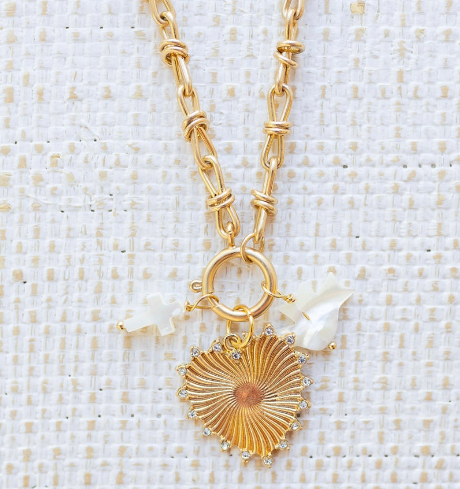 Picture of gold toggle chain with a gold heart pendant trimmed with diamonds. Two additional charms are attached, one a white cross and one a white dove.