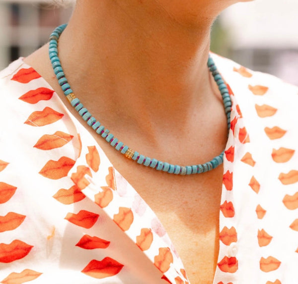 Woman outside wearing a white dress with a red lips print and a blue/gold beaded necklace around her neck