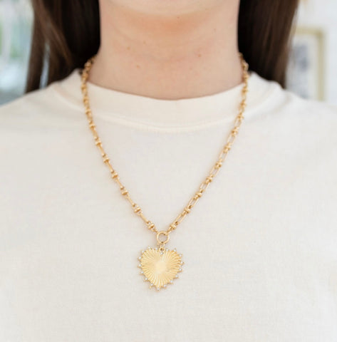 Model wearing a gold toggle chain with a large gold heart pendant.