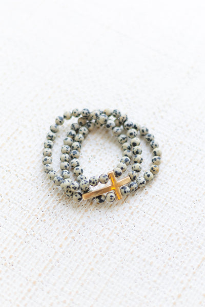 An image of a black and white speckled bracelet stack with a gold cross