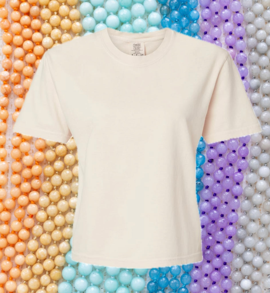 An image of a cream t-shirt with a rainbow colored beaded  background